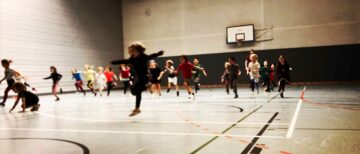 Eine Gruppe Kinder stürmt durch die große Sporthalle.